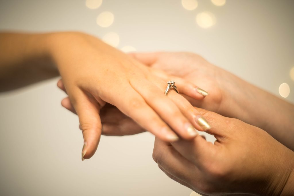 Woman putting engagement on womans finger 1024x683